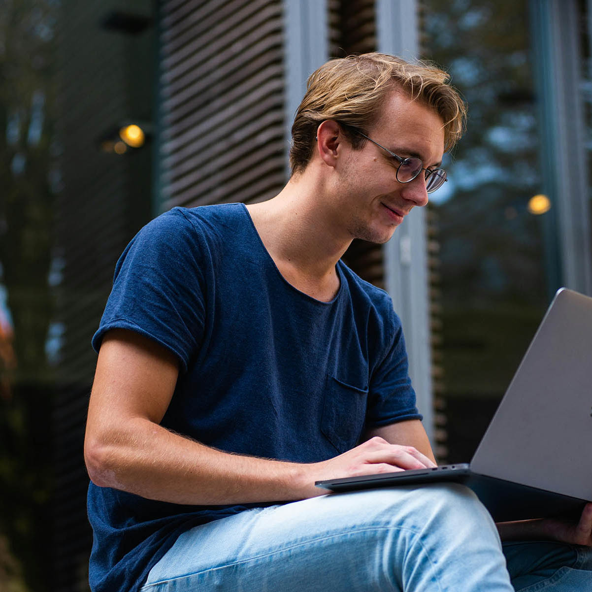 Young man with glasses using a laptop in a public space